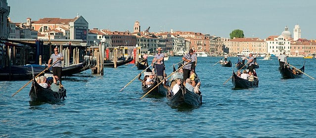 Gondoliers navigating their gondolas with passenger tourists in them in Venice Grand Canal.