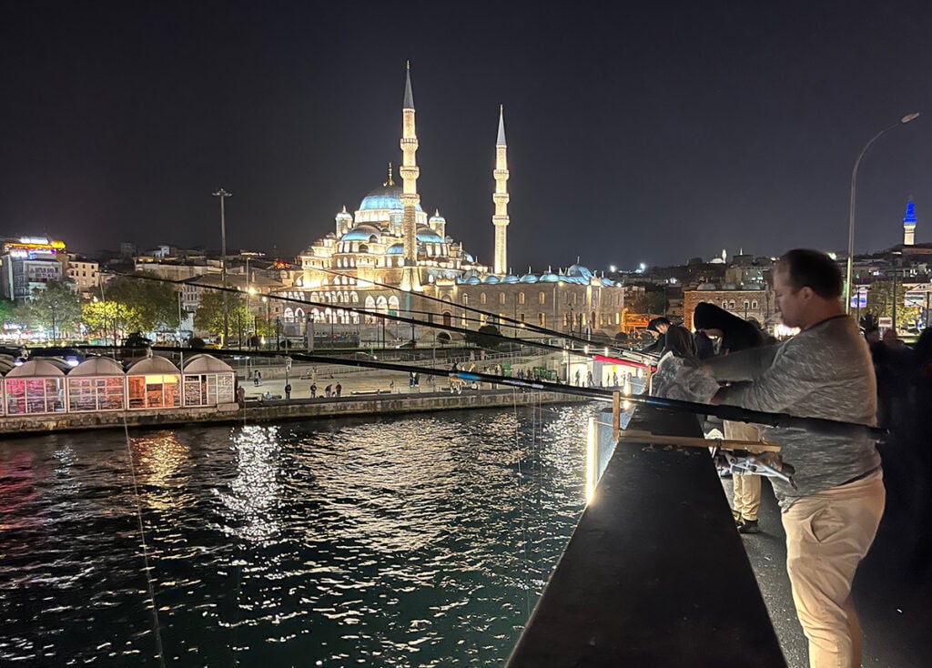 Fisherman on Galata Bridge at night with mosque lit up behind