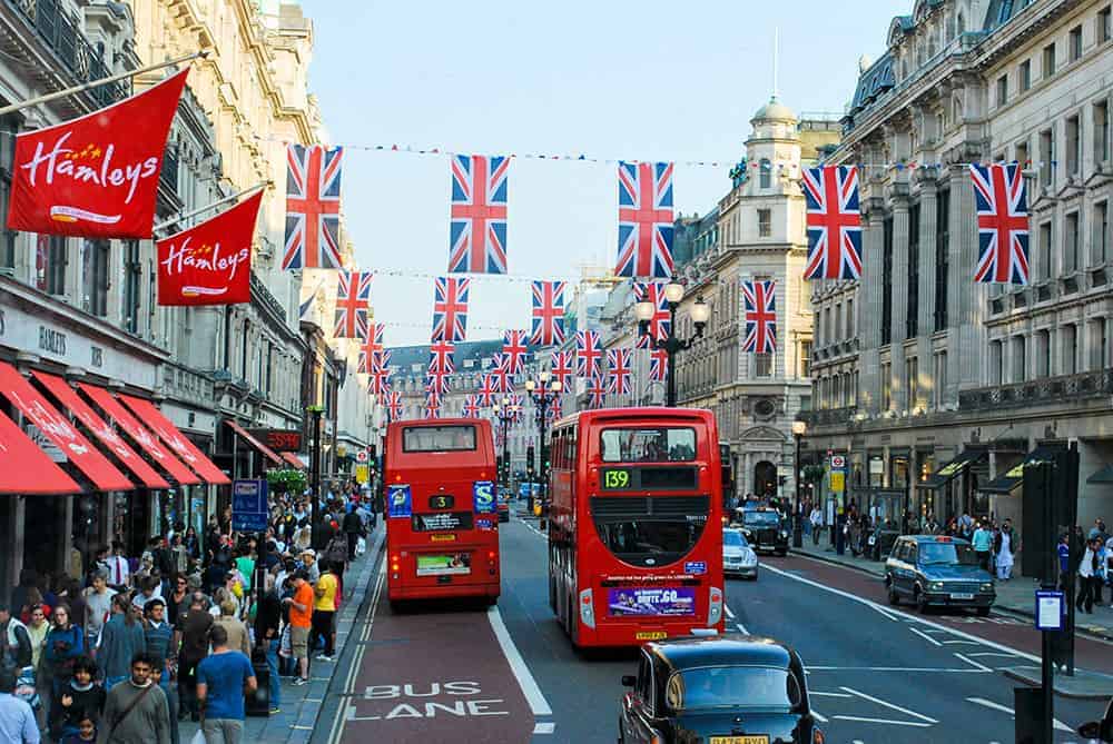 Red buses on Oxford Street, London with streets adorned with national flags, and people crowding on the sidewalk.