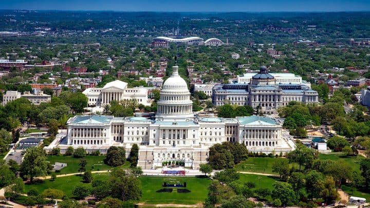 Drone frontal shot of the Capitol Building in Washington, DC, with trees and structures in the surroundings.