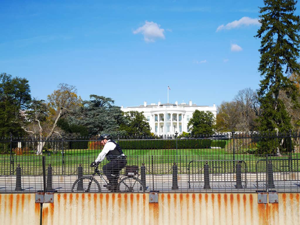 A policeman on a bike passing in the streets in front of the fences of White House.