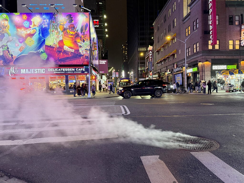 A manhole in the road with steam coming from it in Times Square