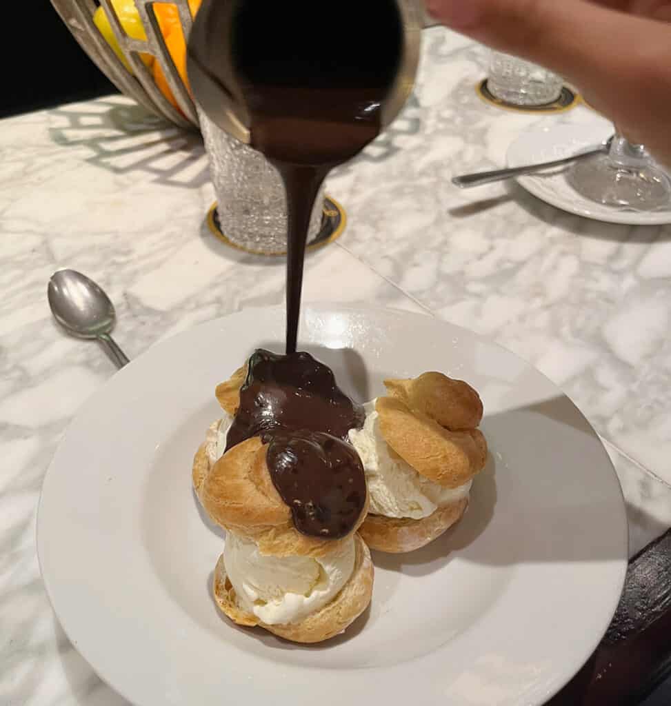 Profiteroles being covered in chocolate sauce
