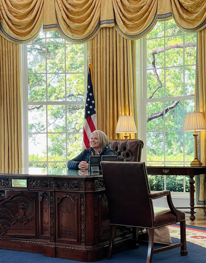 Megan sitting at the desk in the Oval Office replica at The People's House