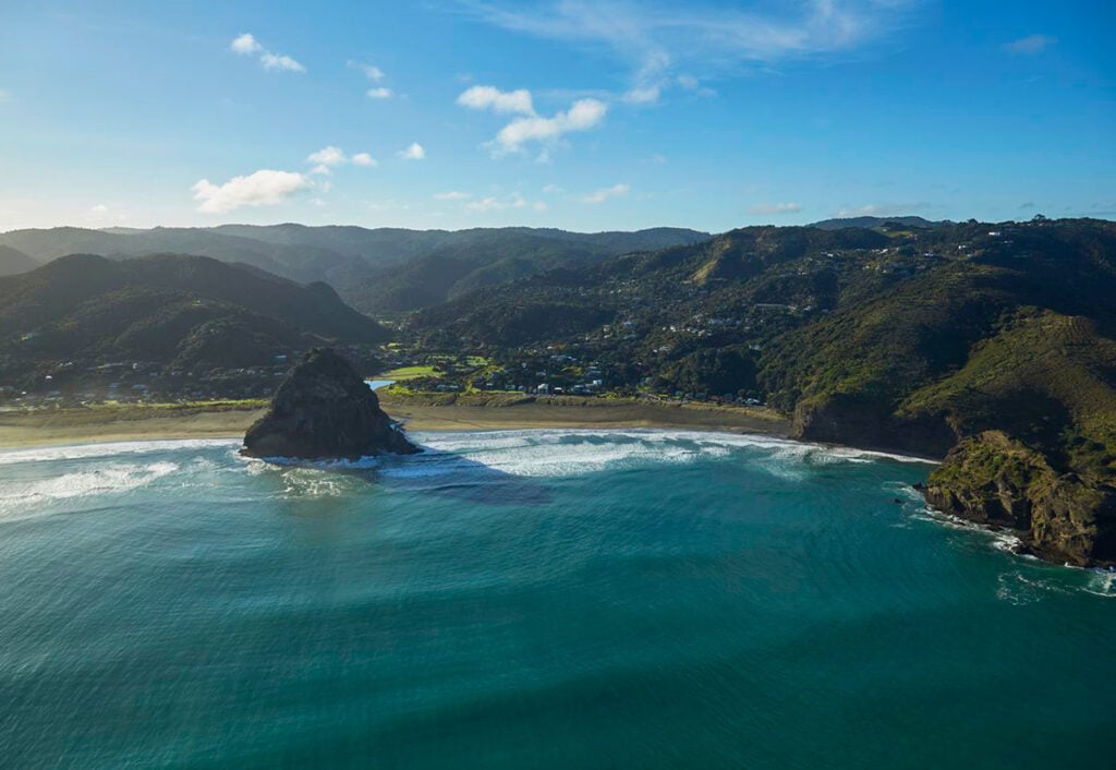 Piha surfing beach with waves crashinh around iconic Lion Rock