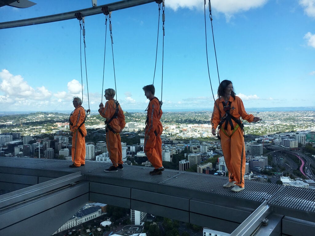 A group in hi-viz overalls and harnesses walk around the Sky Tower ledge
