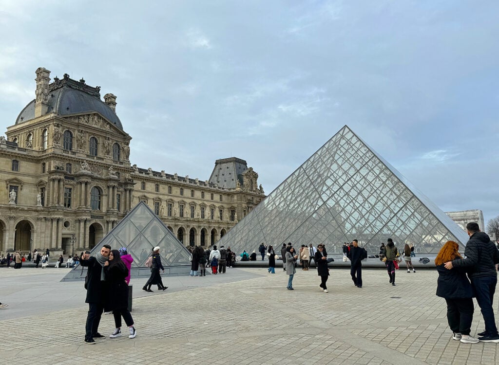 Couples posing in front of the Louvre for selfies