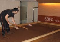 A man using a tool to bury my body with sawdust during my sawdust spa in Taiwan.