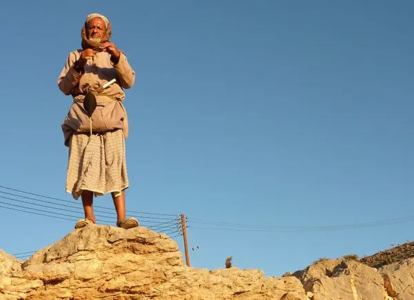 Beduoin Grandad standing on top of a rock and spinning goat hair into yarn.