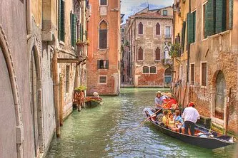 A gondola with tourists discovering Venice while navigating in one of its waterways in the Grand Canal.